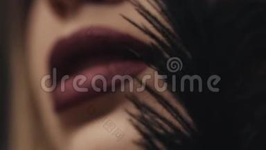 女人的脸部，化妆品的护肤品，化妆品，嘴唇的哑光唇膏，轻轻抚摸的黑色羽毛